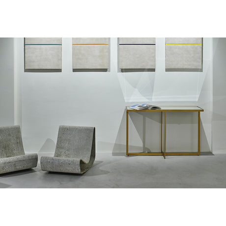 Tablo Bronze Mirrored Glass Console Table with crossed X-frame legs and mirrored top, shown against a gallery wall with framed art and two sculptural concrete chairs.