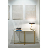 Tablo Bronze Mirrored Glass Console Table with X-shaped legs, styled with books and a table lamp against a light gallery wall with framed art.