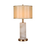 The Calynor 1 Light Column Alabaster Table Lamp features a cylindrical frosted white Spanish alabaster base, brass round pedestal, and beige drum shade. Lamp is off and set against a plain white background.
