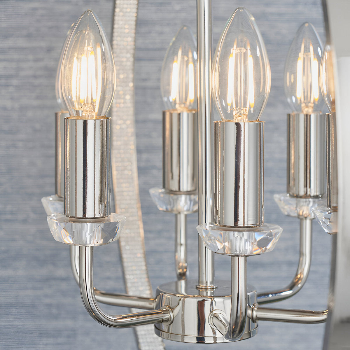 Close-up of the Cliffbury 6 Light Pendant in nickel, showing lit bulbs on cylindrical holders with faceted crystal accents and curved metal arms.