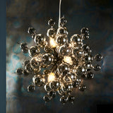 Brockford 9-light cluster pendant in black with smoked mirror and tinted glass spheres on plated metalwork, glowing against a dark textured backdrop.
