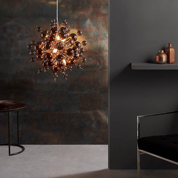 Endon Brockford 9 Light Cluster Pendant in copper with smoked mirror and tinted glass spheres, lit above a side table beside a dark textured wall.