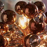 Endon Brockford 9 Light Cluster Pendant in copper, close-up of tinted mirrored glass spheres around a lit E14 candle bulb on plated metalwork.