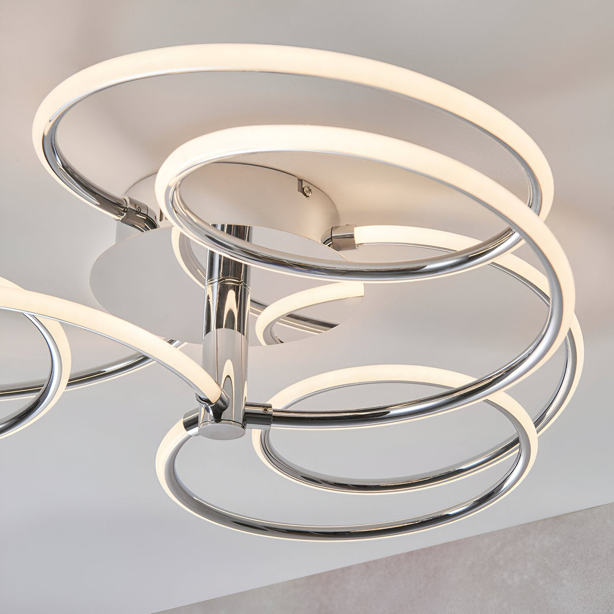 Endon Ravel semi-flush ceiling light in chrome with intertwined illuminated LED rings in a swirling arrangement, shown close-up against a light ceiling.