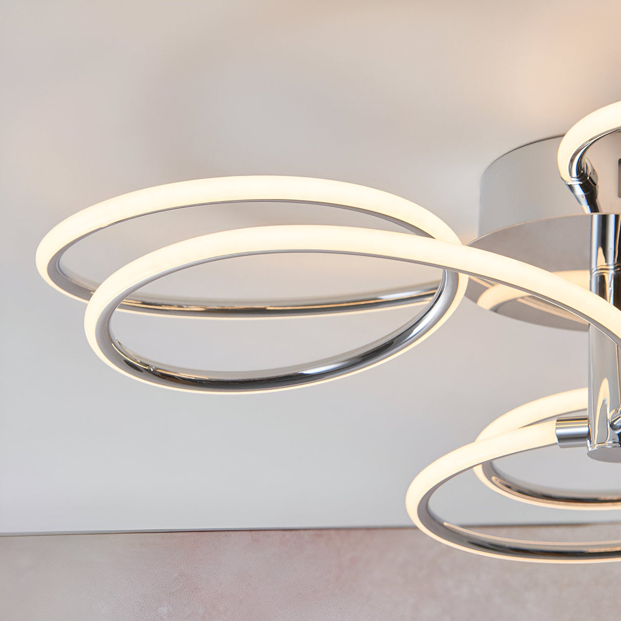 Endon Ravel LED semi-flush ceiling light in chrome, close-up of looping illuminated rings with warm white glow against a neutral ceiling.