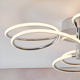 Endon Ravel LED semi-flush ceiling light in chrome, close-up of looping illuminated rings with warm white glow against a neutral ceiling.