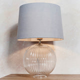Endon Brockdale table lamp with a clear ribbed glass globe base, satin nickel detailing, and tapered grey fabric shade on a light neutral background.