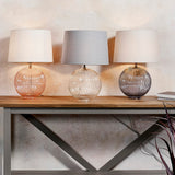 Trio of Endon Brockdale table lamps with ribbed glass bases in pink, clear and smoked grey, topped with tapered fabric shades on a wooden console.