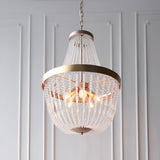 Bevdale 5 Light Pendant in gold, tiered chandelier-style fixture with clear glass beads, hanging from a chain against a white panelled wall.
