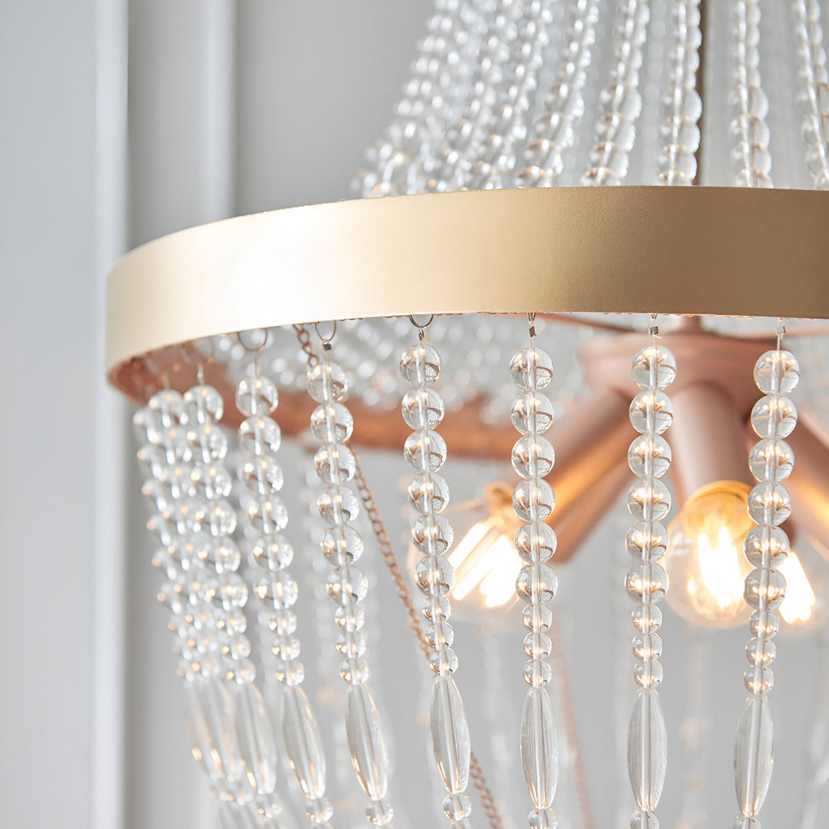 Close-up of the Bevdale 5 Light Pendant in gold, showing a metal ring with clear glass beaded strands and exposed bulbs against a light background.