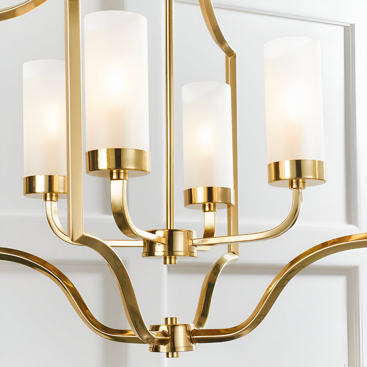 Endon Brackford 4 light pendant in satin brass with frosted glass cylindrical shades on curved arms, shown against a white panelled wall.