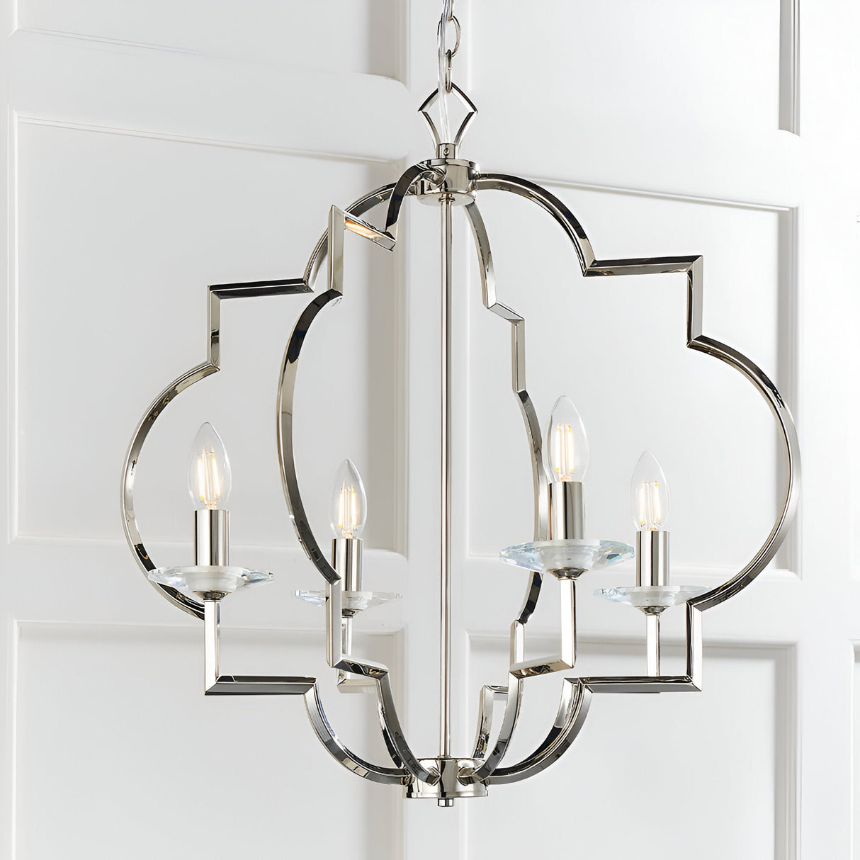 Bramfield 4 Light Pendant in polished nickel with quatrefoil frame, crystal bobeches and candle-style bulbs, hung against a white panelled wall.