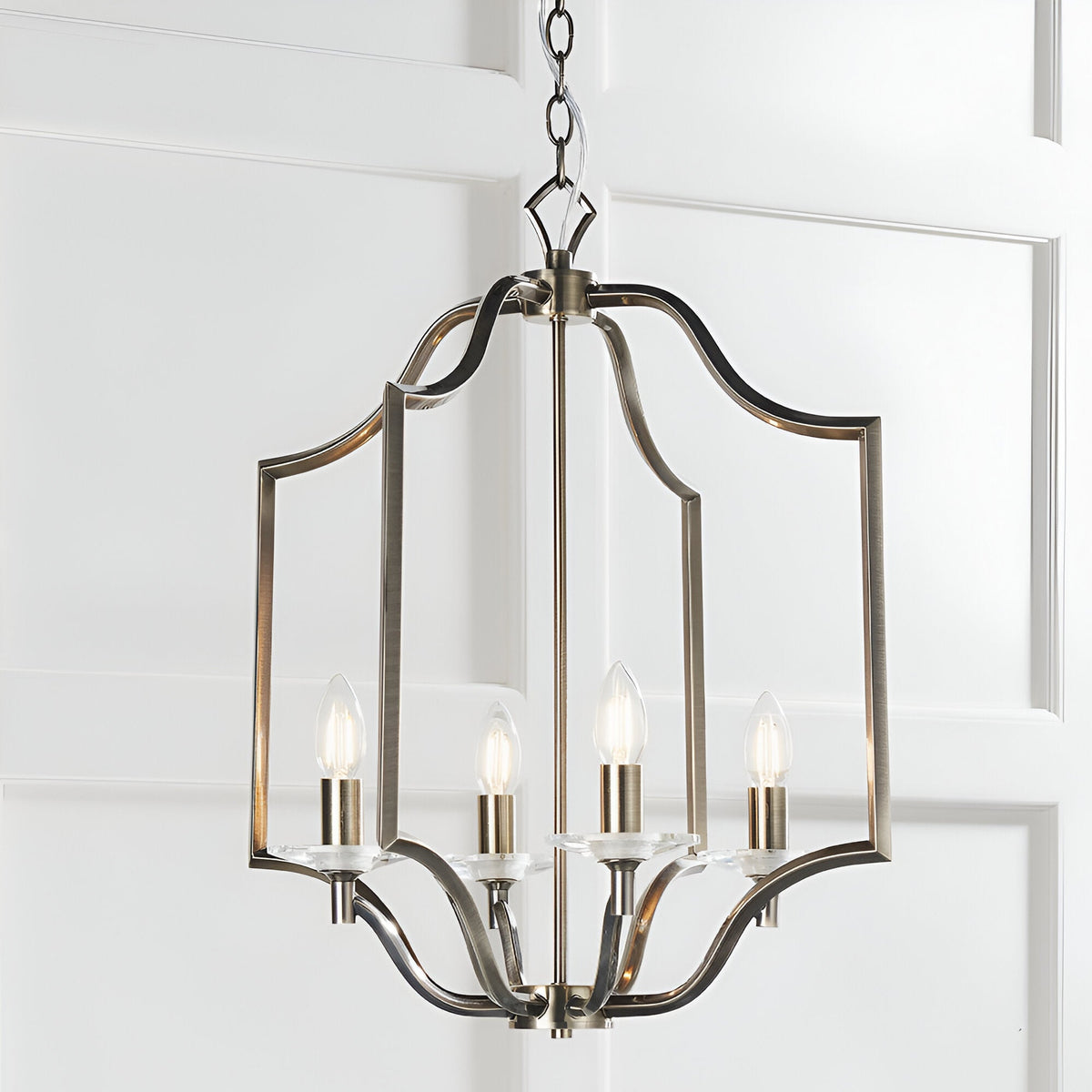 Endon Caldbourne 4 light pendant in antique brass with a curved open lantern frame, four E14 candle bulbs and clear crystal bobeches, chain suspended.