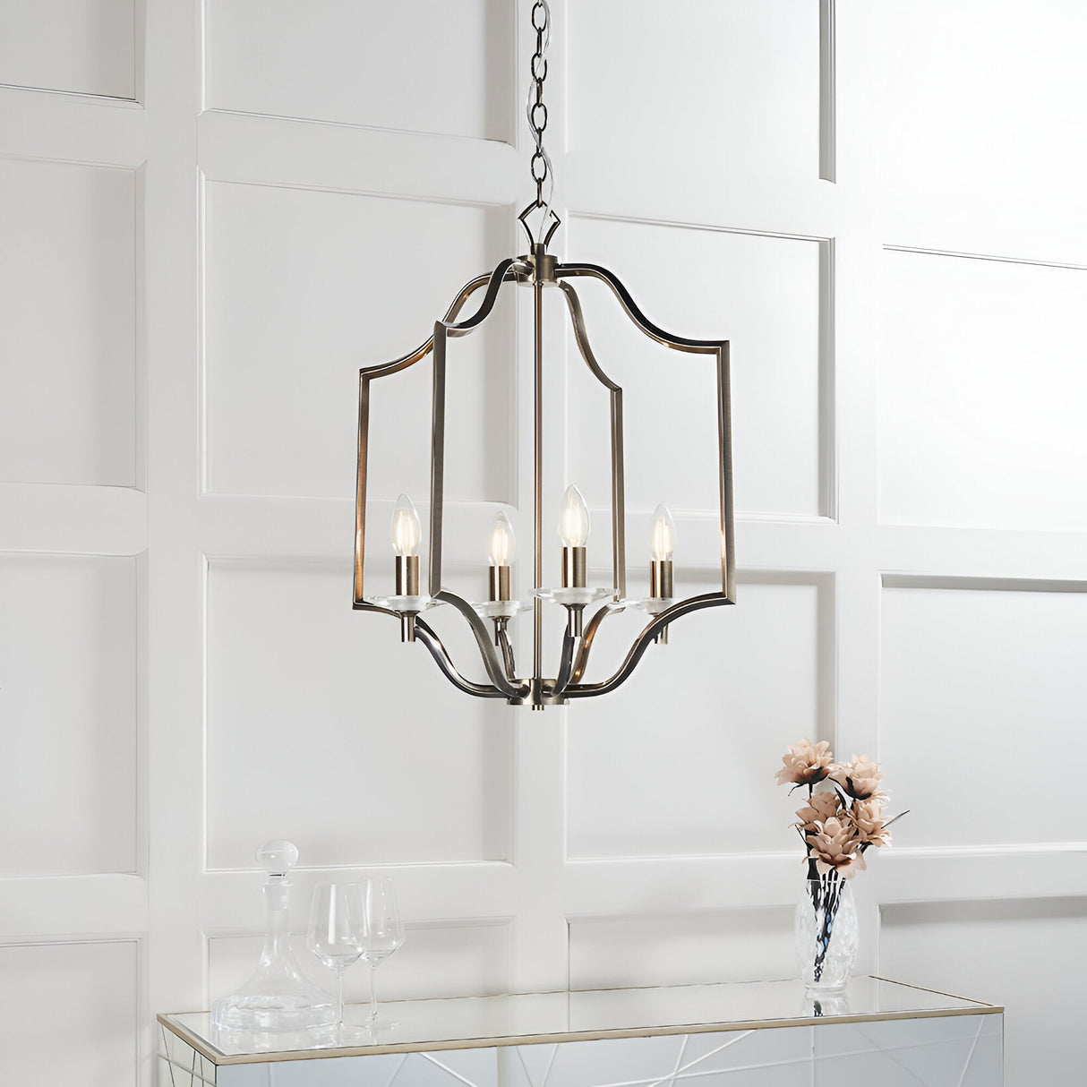Endon Caldbourne 4 light pendant in antique brass with curved open frame and clear crystal bobeches, hung from a chain above a mirrored console.