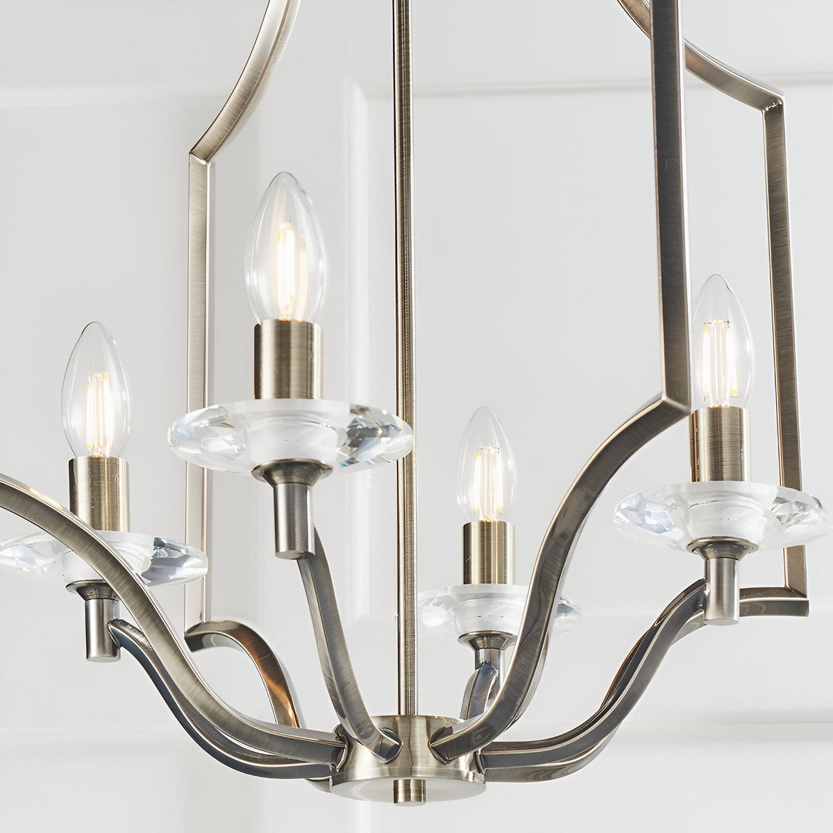 Endon Caldbourne 4 light pendant in antique brass with curved arms, clear K5 crystal bobeches and candle bulbs, shown against a white ceiling.