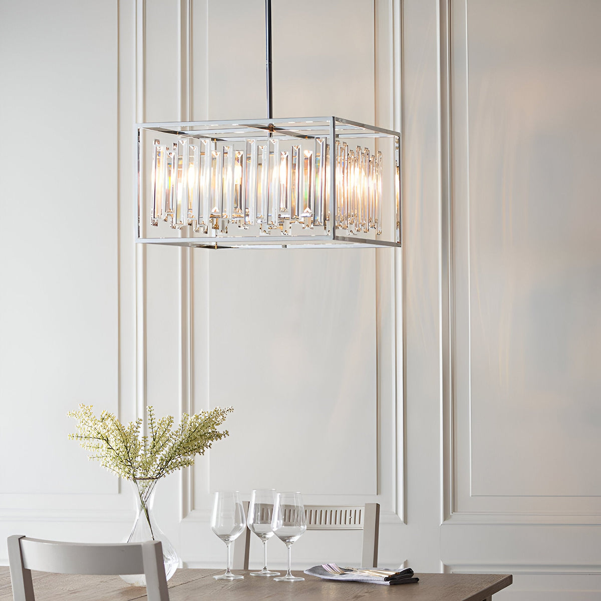Aldbourne 6 Light Pendant in chrome with bevelled crystal glass rods in a rectangular frame, hanging above a dining table in a panelled room.