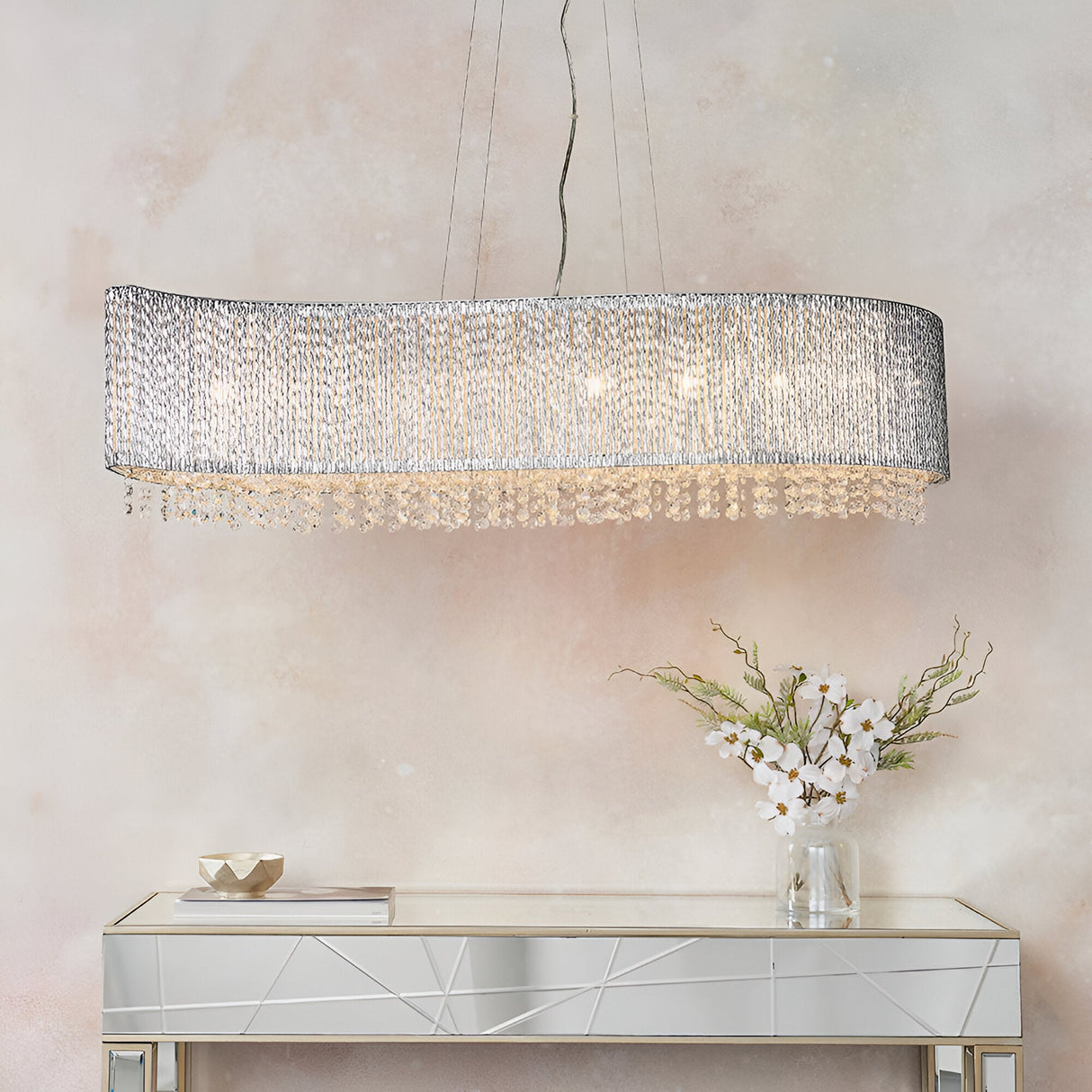 Endon Isadora 8 light linear pendant in polished chrome with twisted rods and clear crystal droplets, hung above a mirrored console with white flowers.
