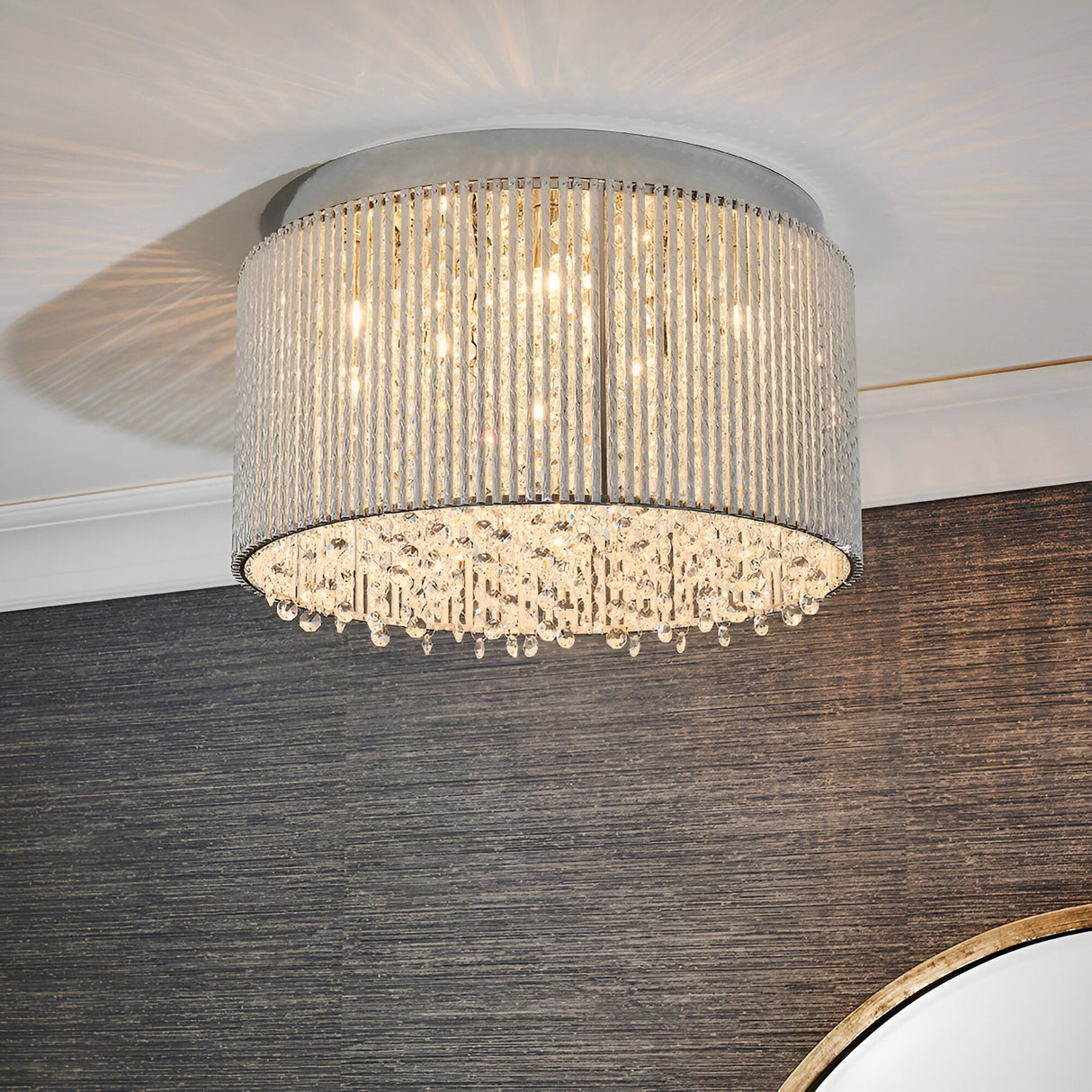 Isadora 10 Light Crystal Flush Ceiling Light in clear, chrome drum frame with hanging crystal droplets, shown fitted to a ceiling above a dark feature wall.