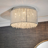 Isadora 10 Light Crystal Flush Ceiling Light in clear, chrome drum frame with hanging crystal droplets, shown fitted to a ceiling above a dark feature wall.