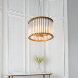 Cliffdale 6 Light Pendant in matt gold, drum-shaped with twisted clear glass rods, hanging above a console table in a panelled white room.