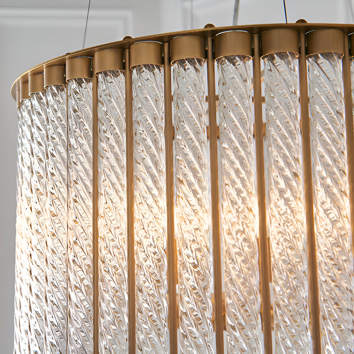 Cliffdale 6 Light Pendant in matt gold, close-up of twisted clear glass rods around a brass frame with glowing warm light inside.
