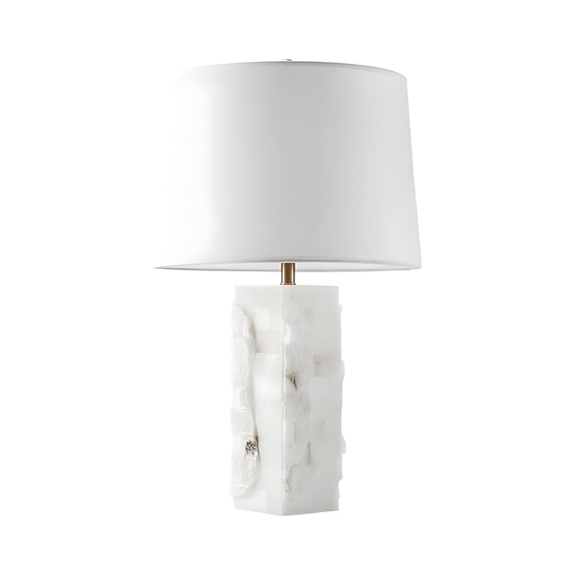 The Kavryn 1 Light Raw Cut Alabaster Table Lamp features a brass and soft white finish, with a textured rectangular alabaster base and a large white drum shade, showcased against a plain white background.