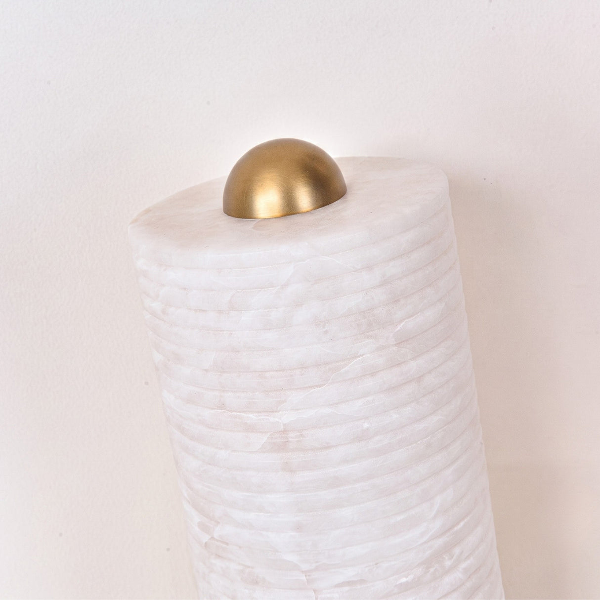 Close-up of the Aurelior Small ribbed alabaster table lamp's domed brass cap atop the horizontally ribbed white stone column, set against a plain light background.