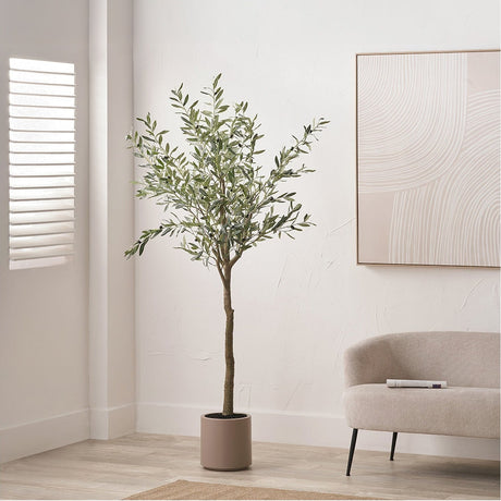 Large Olive Tree in Pot, 210cm faux tree with green foliage in a round beige concrete-style planter, shown in a neutral living room beside a sofa.