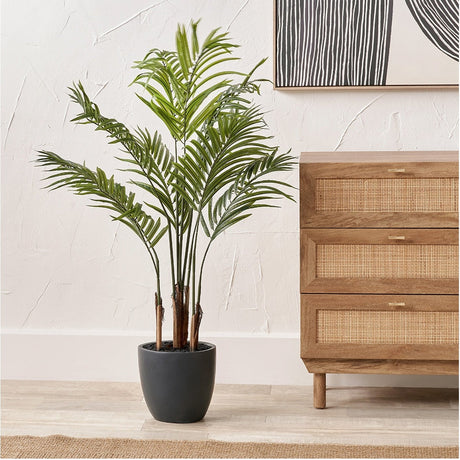 Artificial Areca Palm plant, 120cm, with green fronds in a matte grey pot, styled beside a wood and rattan chest of drawers.