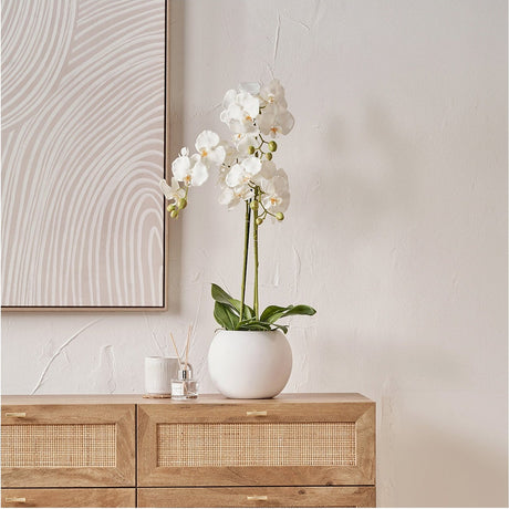 Medium White Orchid in Pot Artificial Plant, 80cm, with white ceramic pot on a wooden sideboard against a light wall.