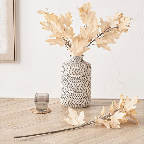 Artificial Apricot Maple Leaf stems, 82cm, in a patterned ceramic vase on a wood floor with an extra loose stem and glass tumbler beside it.