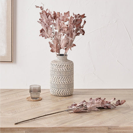 Mulberry Brown Maple Leaf artificial stems, 82cm, arranged in a patterned cream and black textured vase on a wooden table with a single stem laid beside it.