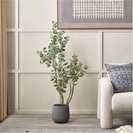 Faux tree in pot, 130cm, with green foliage on multiple stems in a matte grey planter, styled in a living room beside a sofa and framed wall art.