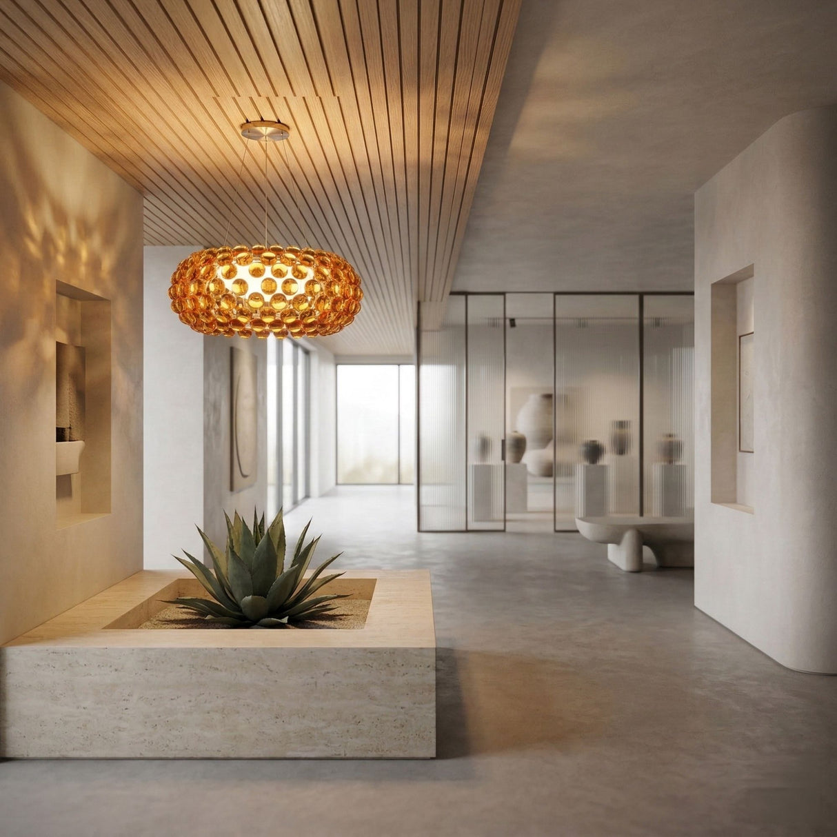 A modern, minimalist interior features a succulent in a central planter, smooth beige walls, wooden ceiling panels, glass partitions with artfully lit vases, and the Briller LED Large Suspension Light in gold as a warm focal point.