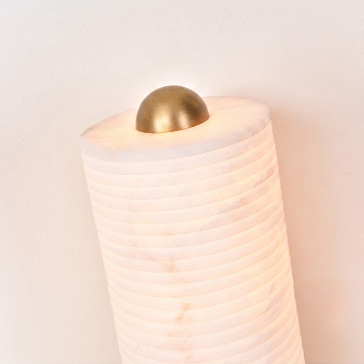 Aurelior Small LED table lamp, close-up of ribbed alabaster column with domed brass cap, glowing warm white from within against a plain light background.