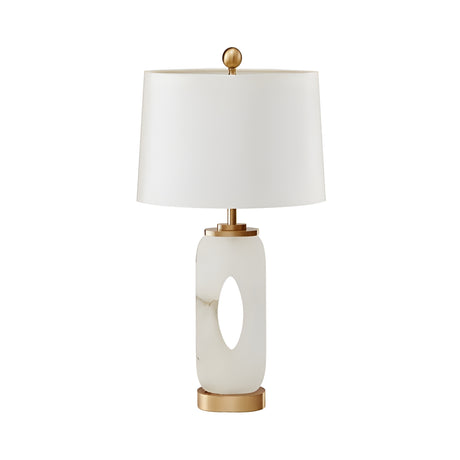 The Elovier 1 Light Carved Oval Alabaster Table Lamp features a soft white oval base with a central cutout, brass accents, and a cylindrical white shade for a modern sculptural look.