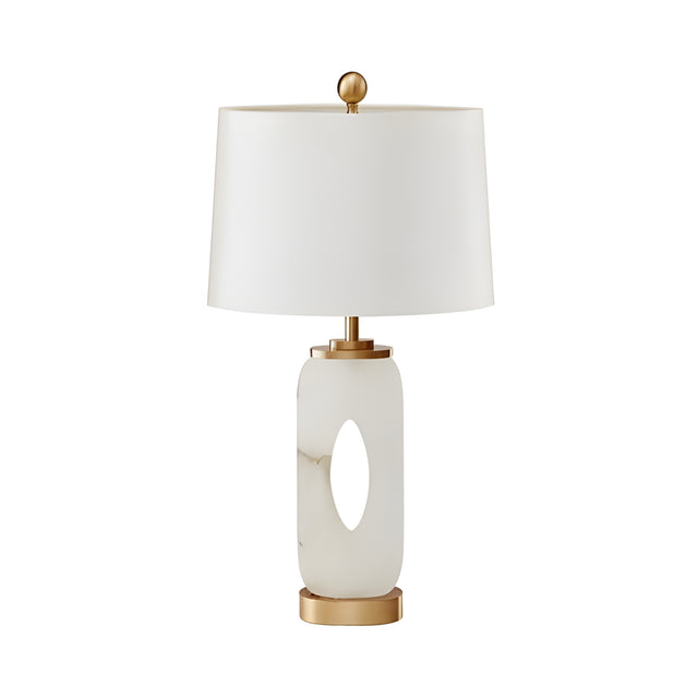 The Elovier 1 Light Carved Oval Alabaster Table Lamp features a soft white oval base with a central cutout, brass accents, and a cylindrical white shade for a modern sculptural look.