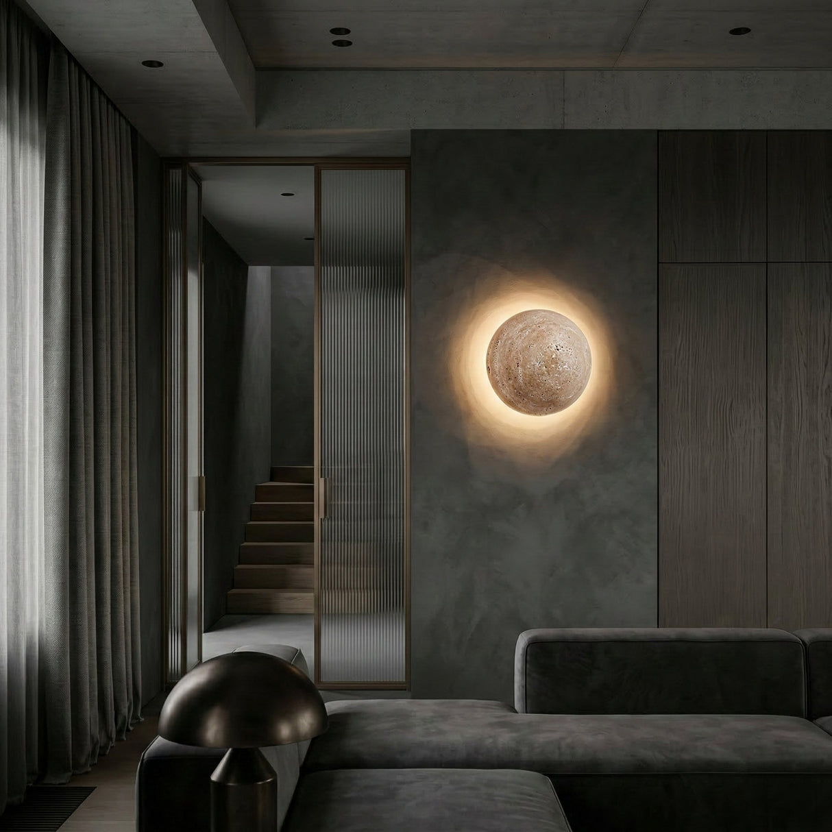 A modern living room with dark walls, a gray sofa, soft drapes, and the Velora LED Spherical Travertine Wall Light in light beige glowing like a moon. A staircase and glass door complete the cozy, minimalist setting.