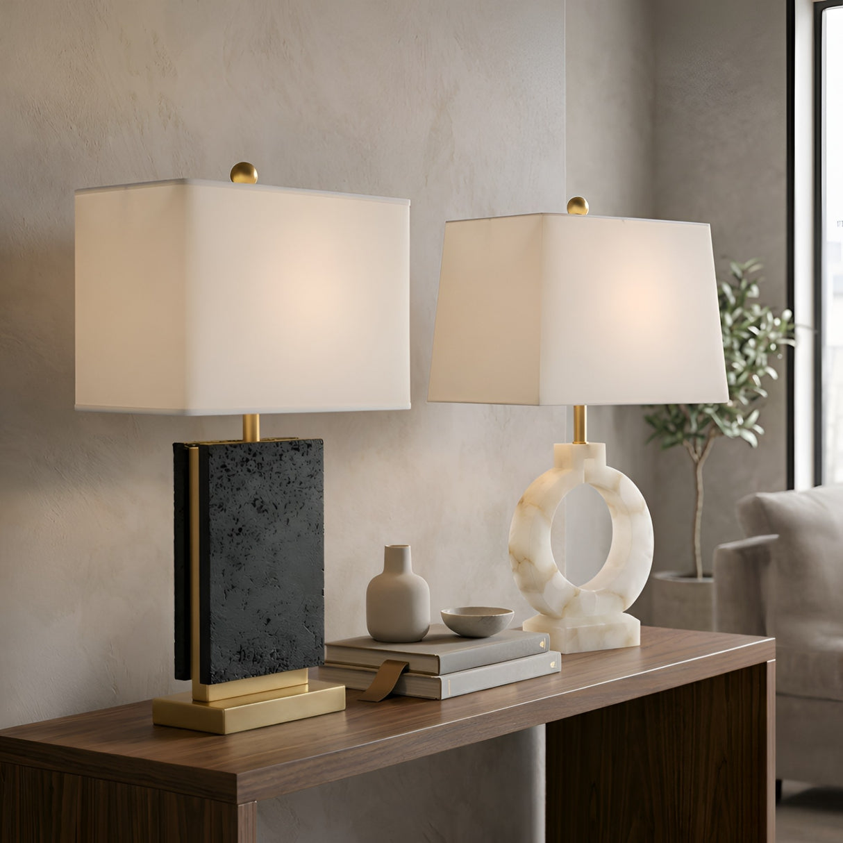 A Forma 1 Light Marble Table Lamp in white and black pairs beautifully with a brass lamp on a wooden console table, complemented by books and small decorative vases for stylish designer lighting.