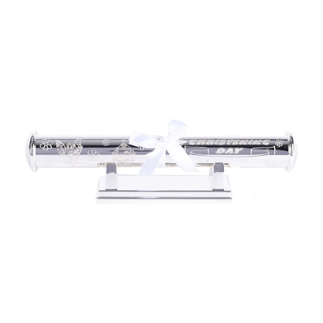 Silverplated tube keepsake box on a low stand, engraved with a cherub, church and flowers, reading "Christening Day", tied with a white ribbon bow, on a plain white background.
