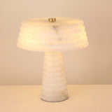 Orivon 3-light table lamp with ribbed tapered alabaster base and banded drum-form shade, brass finial, glowing warm white against a plain background.