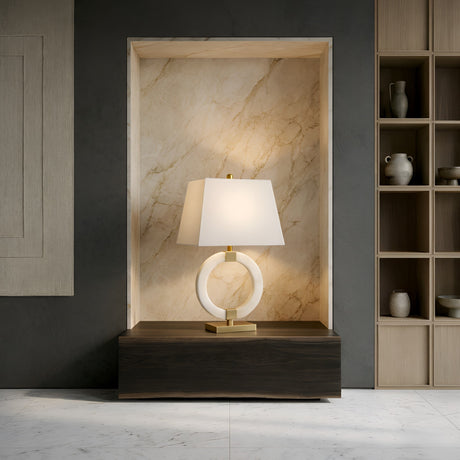 The Calveron 1 Light Circular Framed Alabaster Table Lamp in Brass & Soft White sits on a dark wooden console in a marble alcove, next to shelves holding neutral-toned ceramic vases.