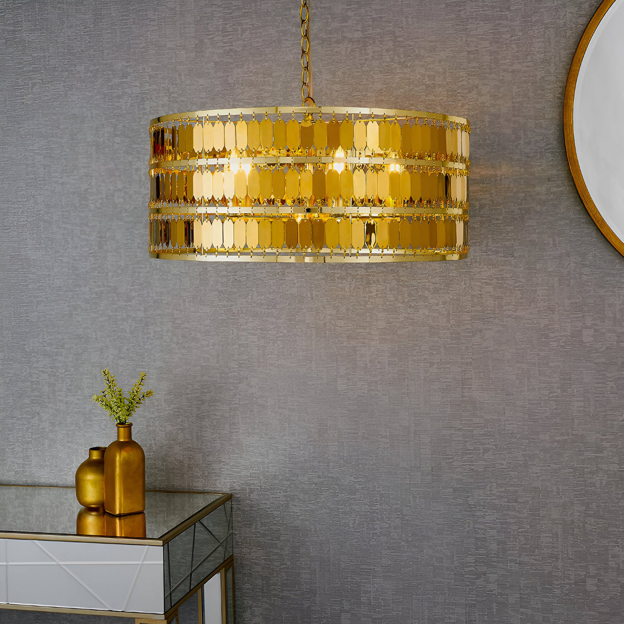 Brackhurst 5 Light Pendant in gold, a drum-shaped fixture with layered hexagonal plates on a chain, hung above a mirrored console table against a grey wall.