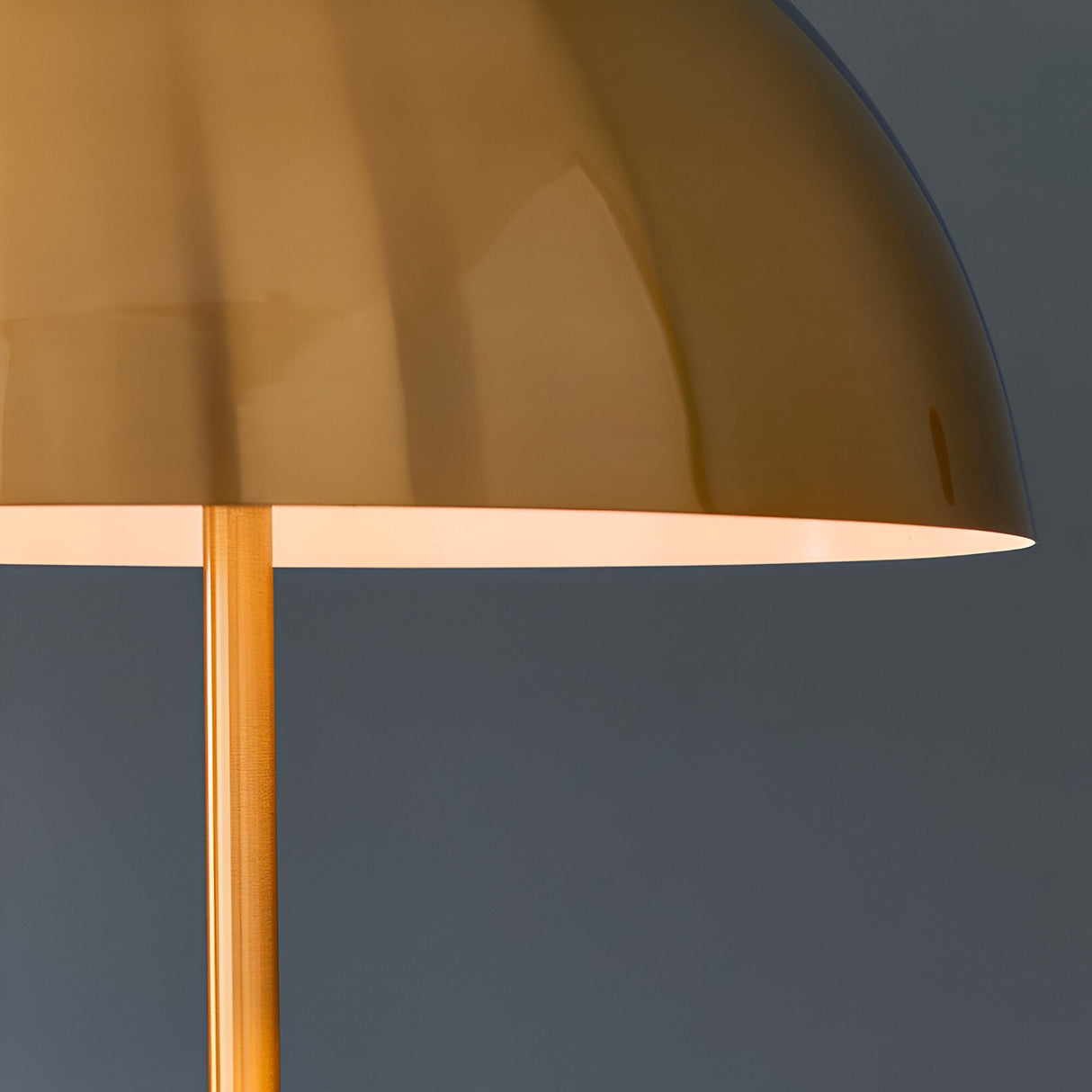 Close-up of the Endon Castford floor lamp showing its antique brass dome shade with gloss white inner and slim brass stem against a grey background.