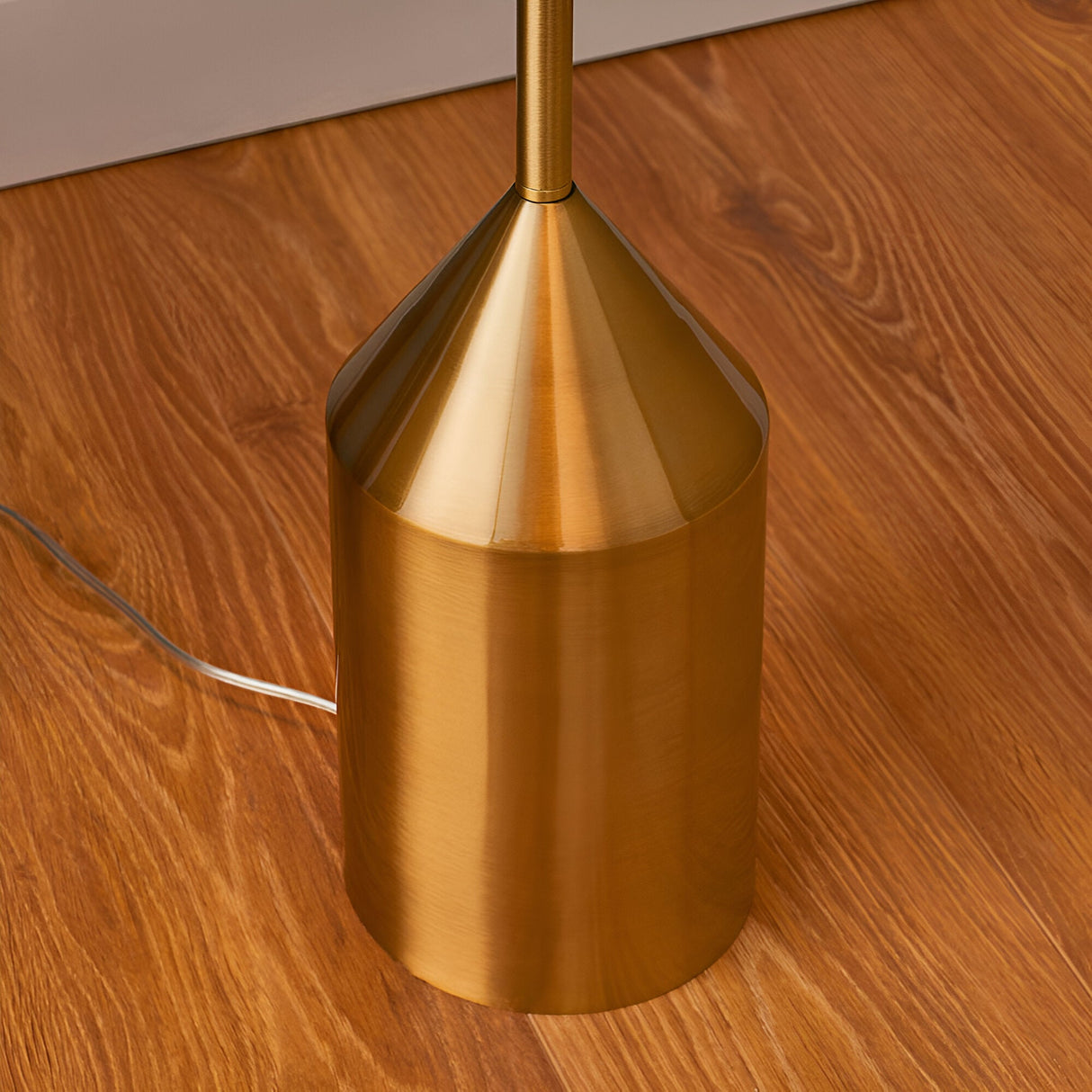 Close-up of the Endon Castford floor lamp base, showing the cylindrical antique brass weight with conical top and slim stem on wood flooring.