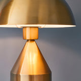 Close-up of the Castford Table Lamp in antique brass, showing the domed metal shade with white gloss interior above a tapered conical base.
