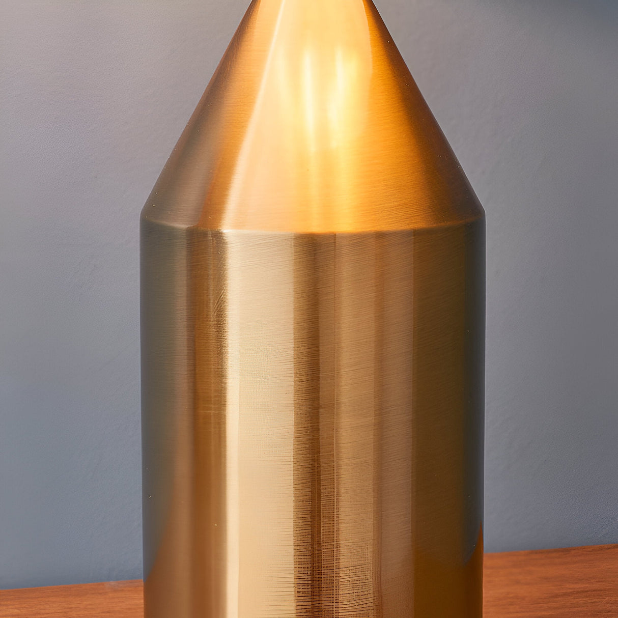 Close-up of the Castford Table Lamp in antique brass, showing its cone-shaped top and cylindrical metal body with a brushed finish against a grey background.