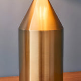 Close-up of the Castford Table Lamp in antique brass, showing its cone-shaped top and cylindrical metal body with a brushed finish against a grey background.