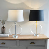 Endon Bramleigh table lamps on a grey sideboard, clear glass ellipsoid bases with nickel and white shade beside brass and black shade.
