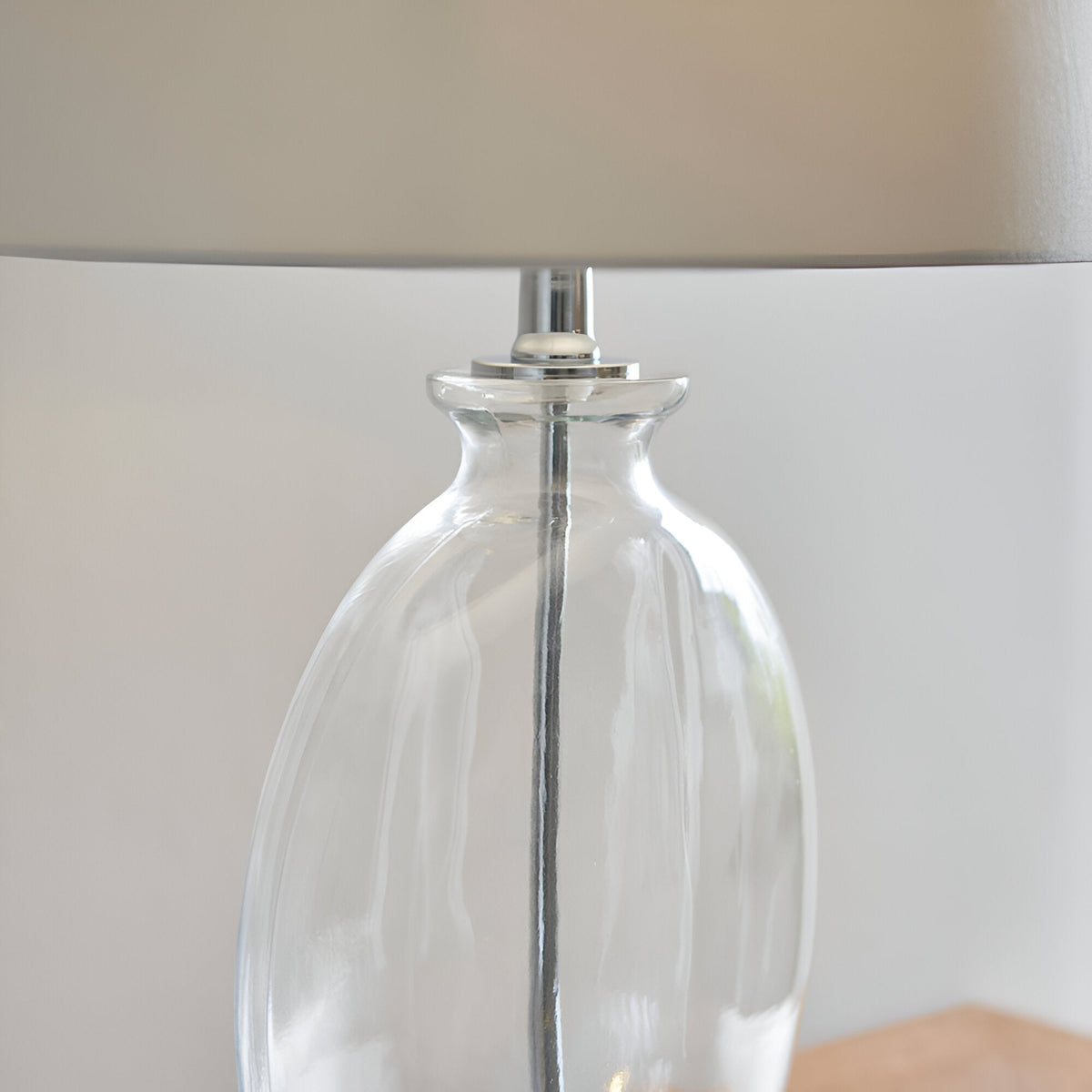 Close-up of the Endon Bramleigh table lamp's clear glass ellipsoid base with polished nickel fitting and white tapered shade above.